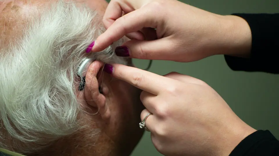 A provider fits a behind-the-ear hearing aid on an older man